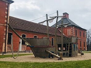 Ein Sandkasten mit einem großen Holzschiff zum Klettern und Spielen. Dahinter steht Schloss Bothmer.