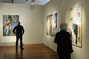 Zwei Besucher betrachten große, bunte Gemälde.
