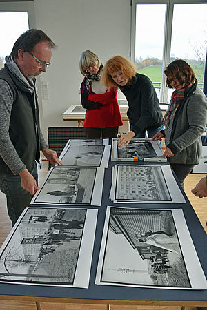 Drei Mitglieder der Kunstkommission und der Fotograf stehen an einem Tisch. Darauf liegen etliche Schwarz-Weiß-Fotografien.