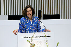 Eine Frau steht an einem Pult und spricht ins Mikrofon.