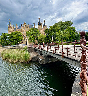 Eine kleine Brücke. Im Hintergrund steht das Schweriner Schloss. 