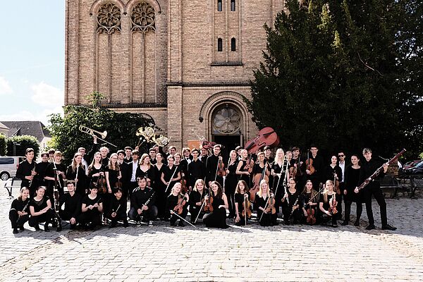 Das Landesjugendorchester posiert in Fürstenberg vor einer Kirche.