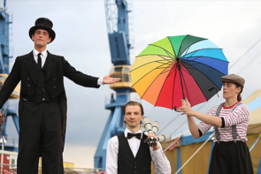 Porträt von drei Künstlern. Einer geht auf Stelzen, einer hat Keulen in der Hand, einer trägt einen bunten Schirm.