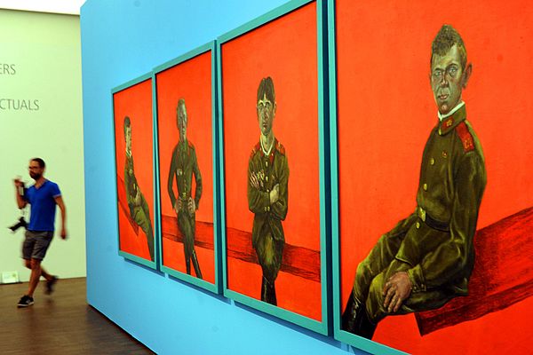Vier Bilder hängen nebeneinander. Ein Soldat sitzt in wechselnden Posen vor einem roten Hintergrund. 