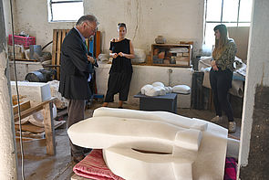 Mitglieder der Kunstkommission stehen mit Alexandra Lotz im Atelier und betrachten Skulpturen.