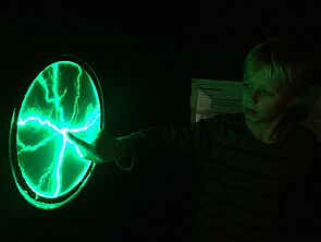 Ein Finger tippt auf eine runde Scheibe und löst grüne Blitze aus.