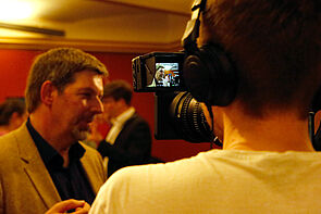 Ein Mann wird interviewt. Rechts ist der Kameramann zu sehen.