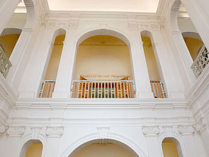 Das Treppenhaus besteht aus weißen Säulen und weißen Wänden mit offenen Rundbögen.