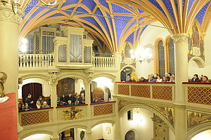 Innenansicht der Schlosskirche. Mit hellen Emporen, blauer Gewölbedecke und der Orgel. Auf den Emporen sitzen Menschen.