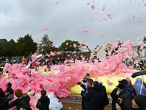 Viele Menschen stehen um ein großes Feld aus rosa Schaum. Flocken fliegen durch die Luft.
