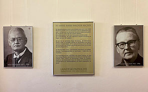 An einer Wand hängt ein Porträt von Walter Karbe und Annalise Wagner. Dazwischen befindet sich eine Infotafel.