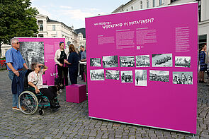 Ein Mann und eine Frau im Rollstuhl betrachten die Ausstellung.