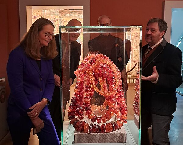 Vier Personen im Museum. Sie stehen vor einem Ausstellungsstück: Ketten aus Bernstein.