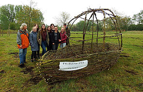 Acht Jugendliche und stehen mit Ines Diederich vor einem Schiff, das sie aus Weidenästen gefertigt haben.