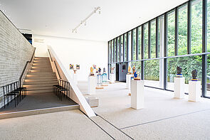 Ein Ausstellungsraum. Mehrere Skulpturen stehen dort verteilt. Eine Treppe führt nach oben.