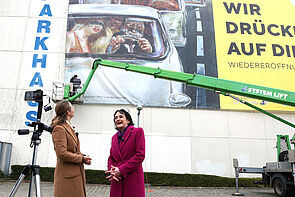 Das Plakat ist 22 mal 12 Meter groß. Davor stehen zwei Frauen. Bettina Martin und Dr. Pirko Kristin Zinnow.