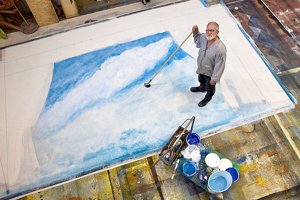 Ein Mann steht auf einer großen, weißen Flächen und malt in Blau.