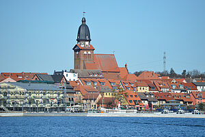 Wasser. Dahinter zeigt sich die Altstadt von Waren. Eine Kirche ragt aus den Gebäuden hervor.