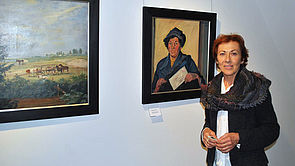 Sabine Kliefert steht vor einer weißen Wand, an der zwei Bilder hängen.