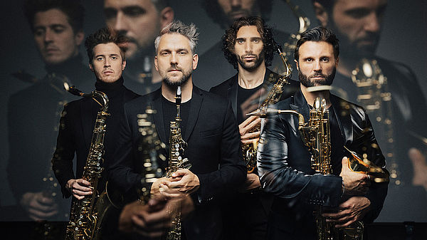 Vier Musiker, gekleidet in Schwarz, in den Händen halten sie ihre Musikinstrumente.