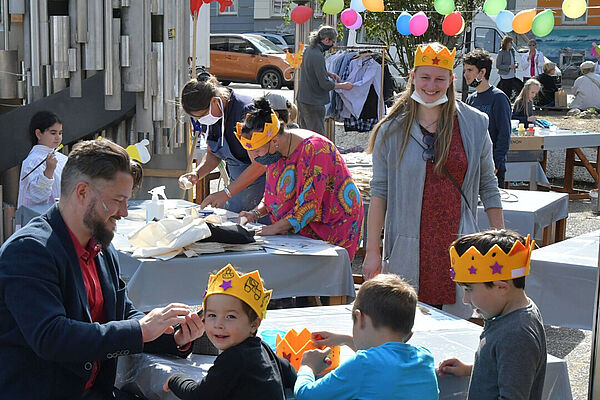 Mehrere Menschen tragen gelbe Filzkronen, schminken Kinder und feiern.