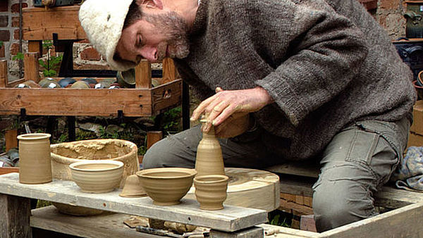 Ein Mann sitzt an einer Töpferscheibe und töpfert eine Vase.