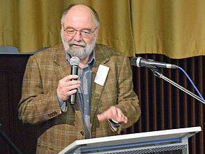 Jürgen Seidel steht mit einem Mikrofon in der Hand an einem Rednerpult.