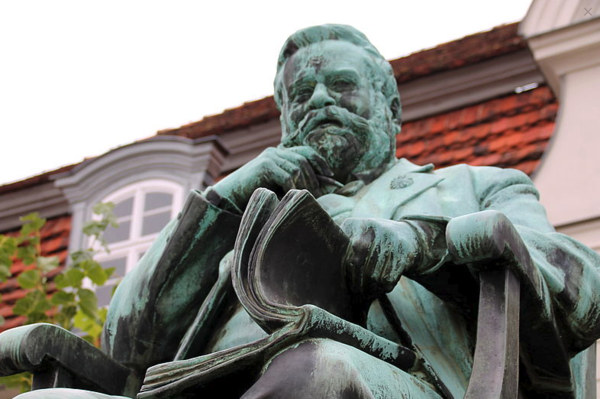Ein Denkmal von Fritz Reuter. Er sitzt auf einem Stuhl und Blättert in einem Buch.