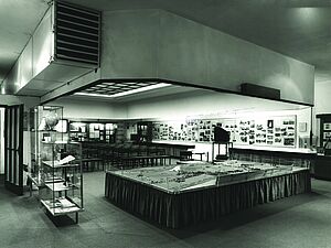 Ein Ausstellungsraum. Im Raum stehen Vitrinen mit Exponaten. An den Wänden hängen Glaskästen mit Fotos. In der Mitte steht ein Modell der Anlage.
