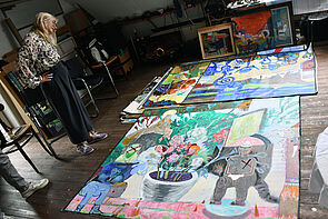 Eine Frau steht im Atelier. Auf dem Boden liegen großformatige Bilder.