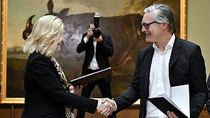 Manuela Schwesig und Alexander Otto stehen einander gegenüber und reichen sich die Hand. Im Hintergrund steht ein Fotograf und fotografiert. An der Wand hängt ein großes Gemälde von Nashorn Clara.