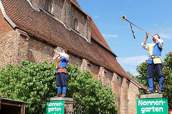 Ein Backsteinhaus. Es gehört zum Kloster Rehna. Vor dem Eingang stehen zwei Menschen. Sie tragen historische Kostüme.