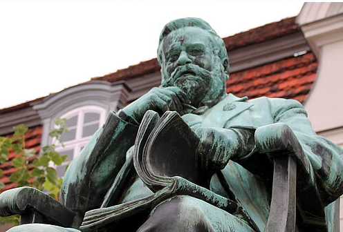 Ein Denkmal zeigt einen Mann, der in einem Buch blättert. Der Mann ist Fritz Reuter.