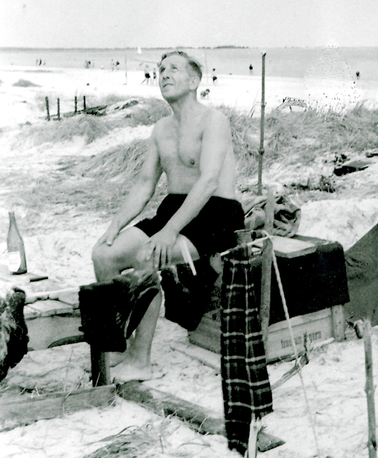 Ein Mann in Badehose sitzt auf einer Kiste am Strand.