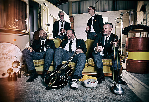 Fünf Musiker der Band The Sazerac Swingers im Probenraum. Drei sitzen auf dem Sofa, zwei stehen dahinter.