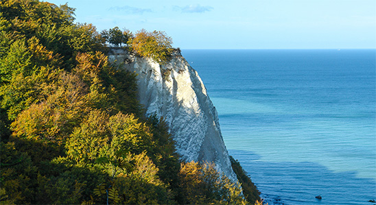 Ein weißer Felsen. Vor ihm ist die Ostsee. Neben dem Felsen stehen viele Bäume. 