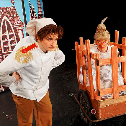 Zwei Schauspieler. Ein Schauspieler ist Zwerg Nase. Der andere Schauspieler ist ein Mädchen. Es sitzt in einem Käfig.